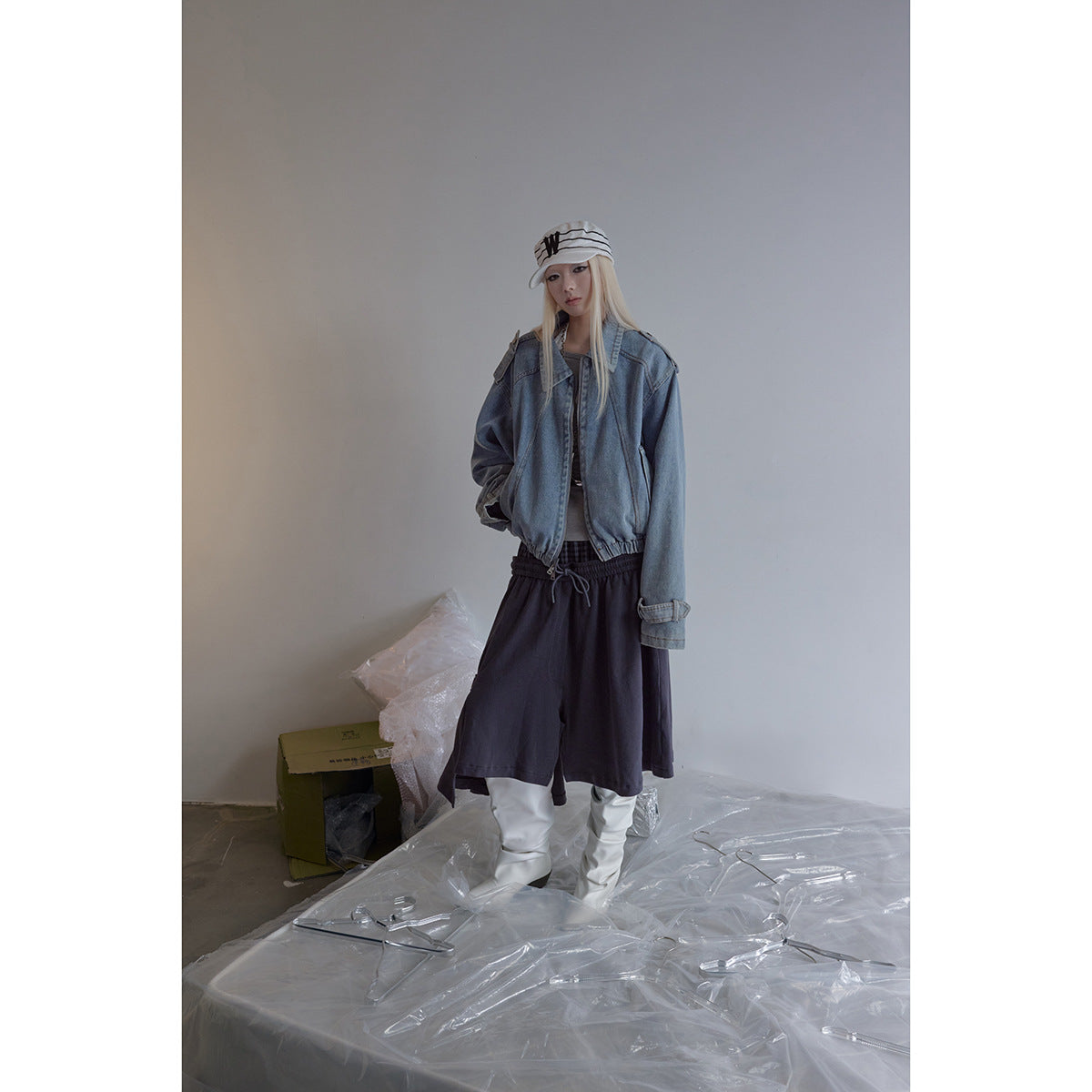 Model wearing a cropped blue denim zip jacket with a white top, dark skirt and white boots.