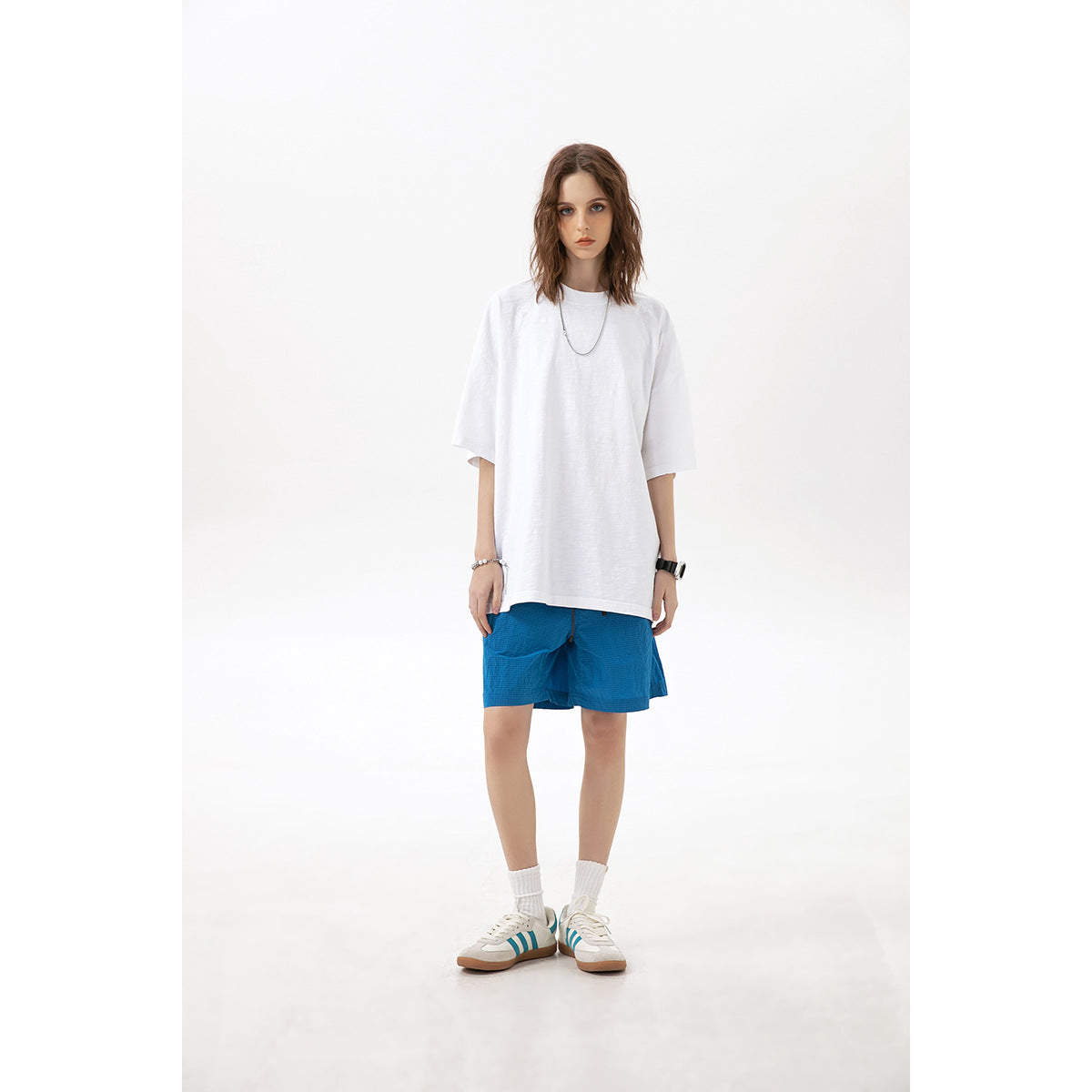 Model wearing an oversized plain white T-shirt and bright blue shorts against a white studio background.