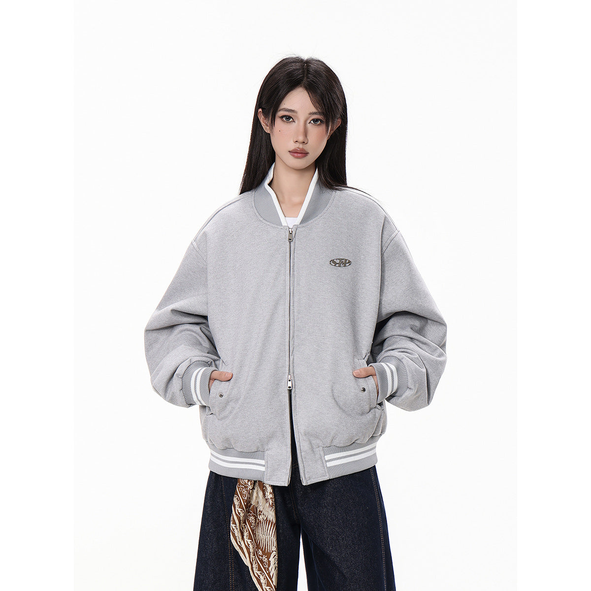 Model wearing an oversized light gray zip-front bomber jacket with striped ribbed cuffs and hem, front pockets, and a small