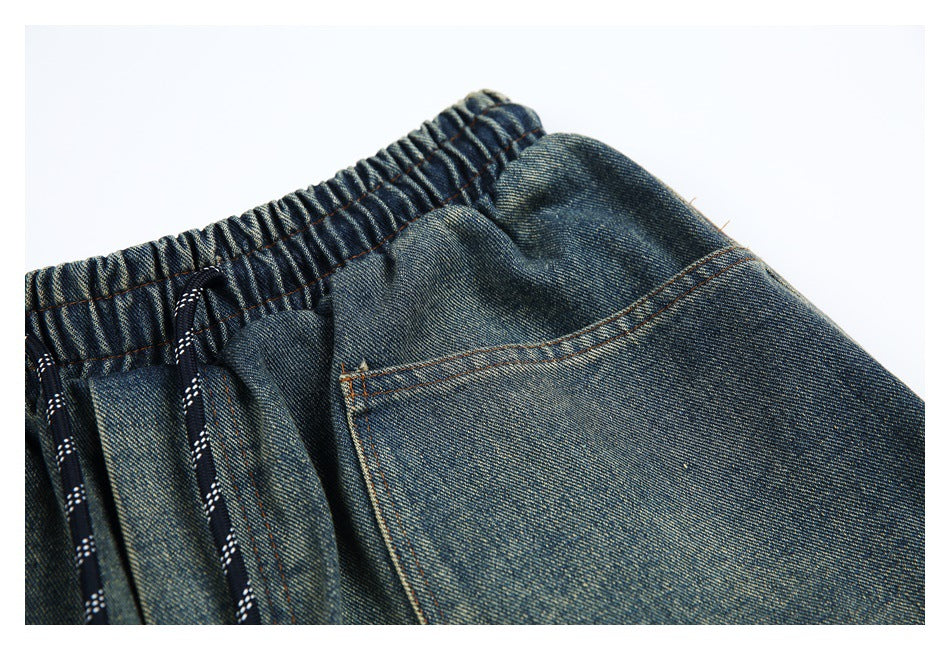Close-up of faded blue denim shorts showing the elastic waistband, drawcord, and a stitched pocket.