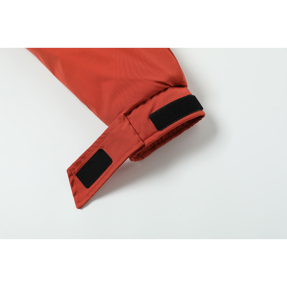 Close-up of a rust-red jacket cuff with adjustable black hook-and-loop tabs.