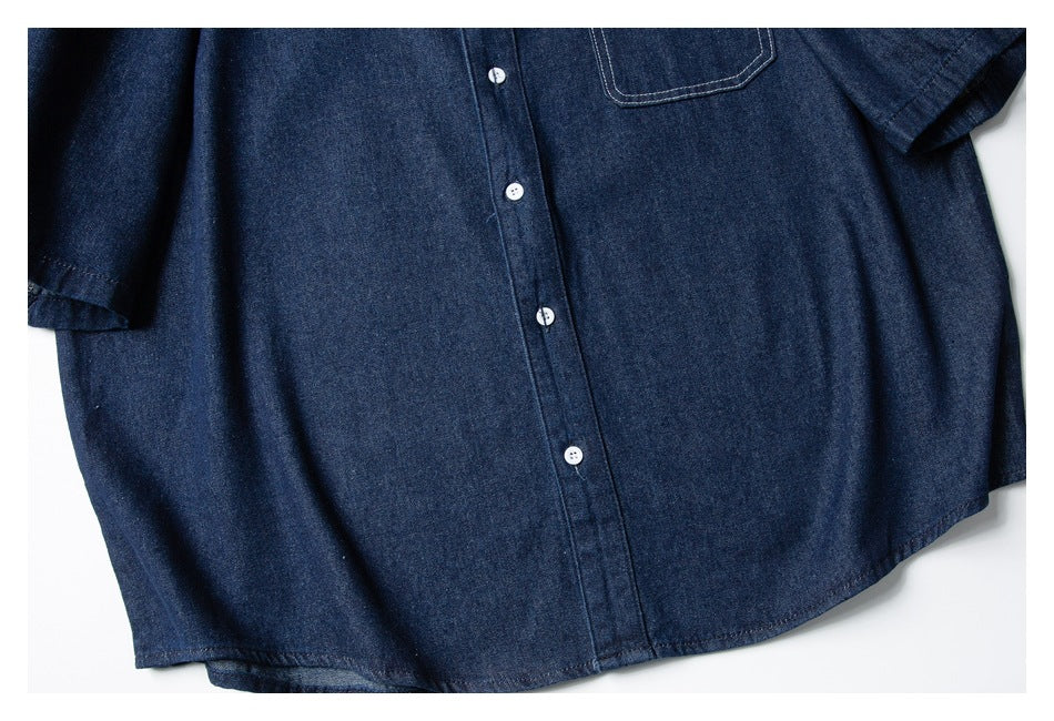Close view of a dark indigo button-front shirt with white buttons and a stitched chest pocket, laid flat.