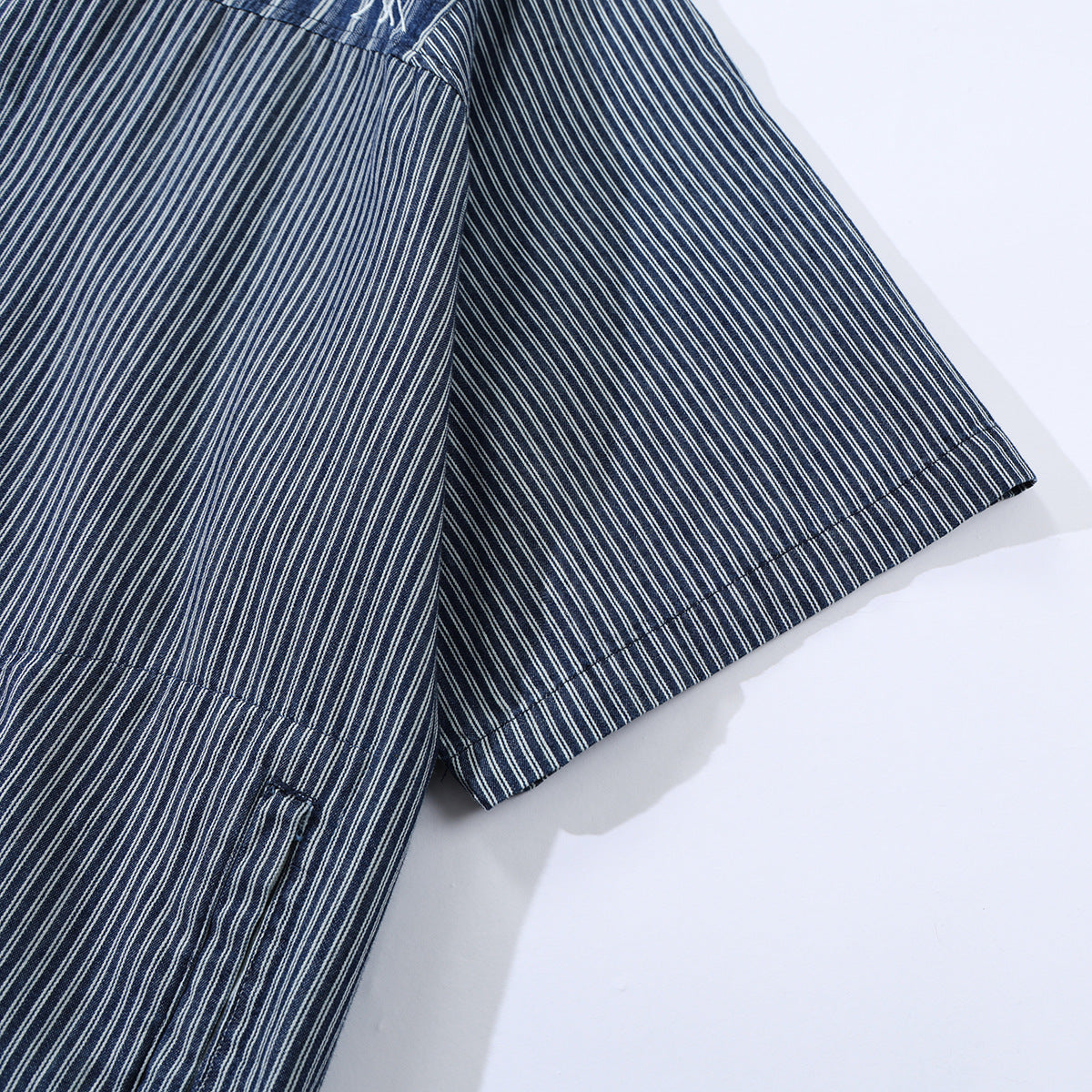 Cropped view of a short sleeve and body of a dark blue shirt with fine white vertical stripes.