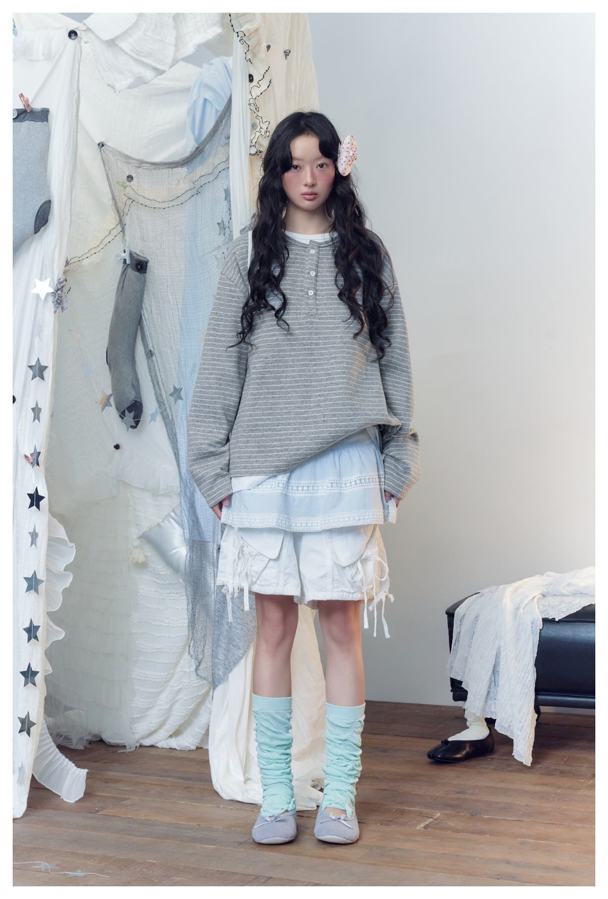 Model wearing gray striped Henley top over a white layer with a light blue skirt and white shorts