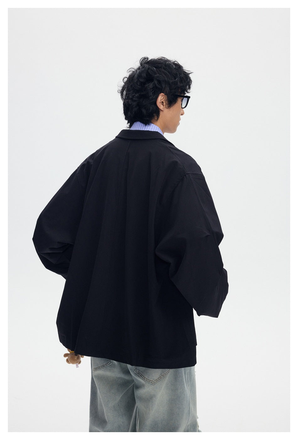 Rear view of a model wearing an oversized black blazer with a center back seam and loose gray jeans.