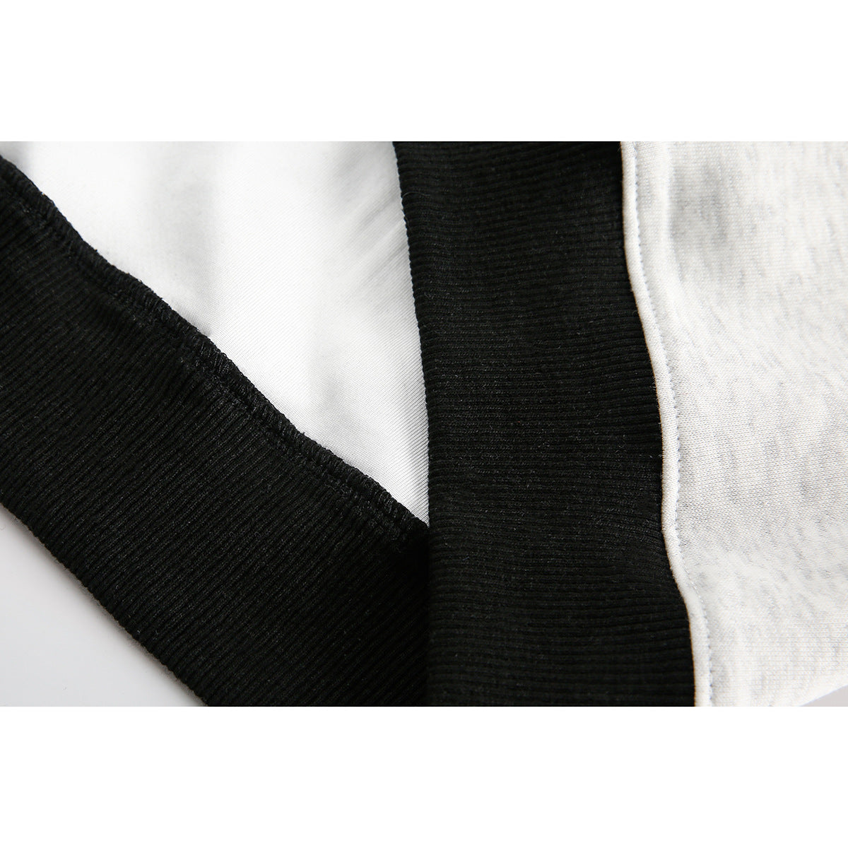 Close-up of black ribbed trim beside light-gray hoodie fabric, showing the seam and edge stitching.