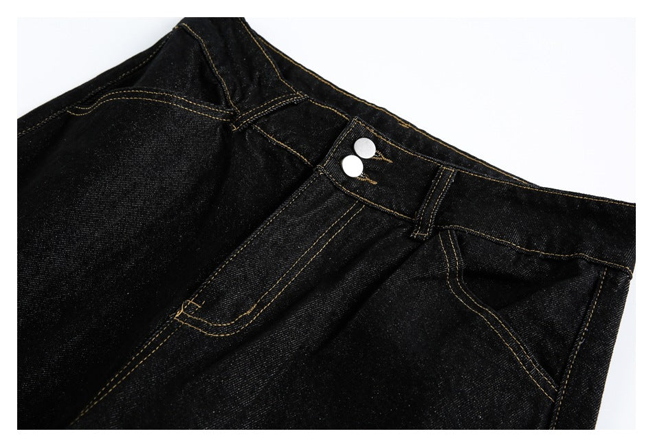 Close-up of the black jeans' waistband, double-button closure and curved front pocket with gold stitching.