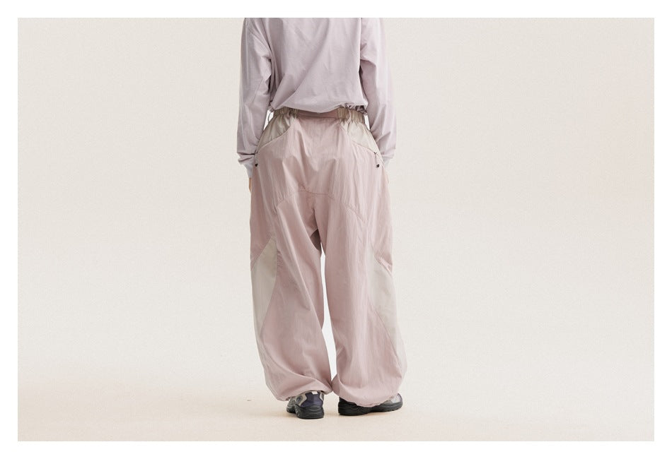 Back view of a model wearing pale mauve wide-leg pants with light contrasting panels and gathered cuffs.