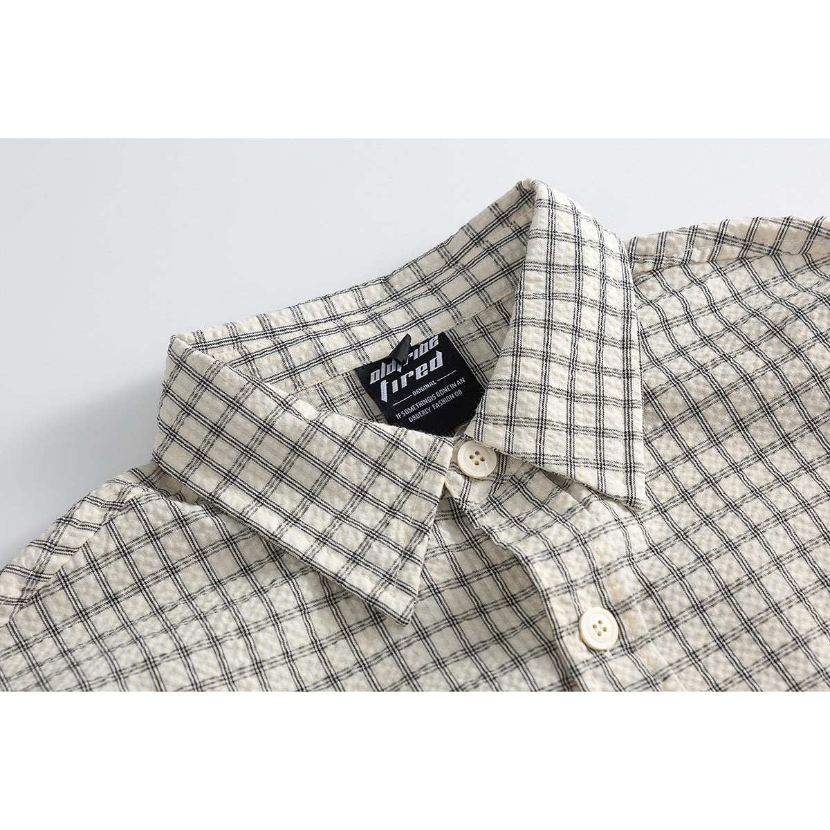 Close-up of a cream plaid button-up shirt showing its collar, placket, buttons, and sewn-in neck label.