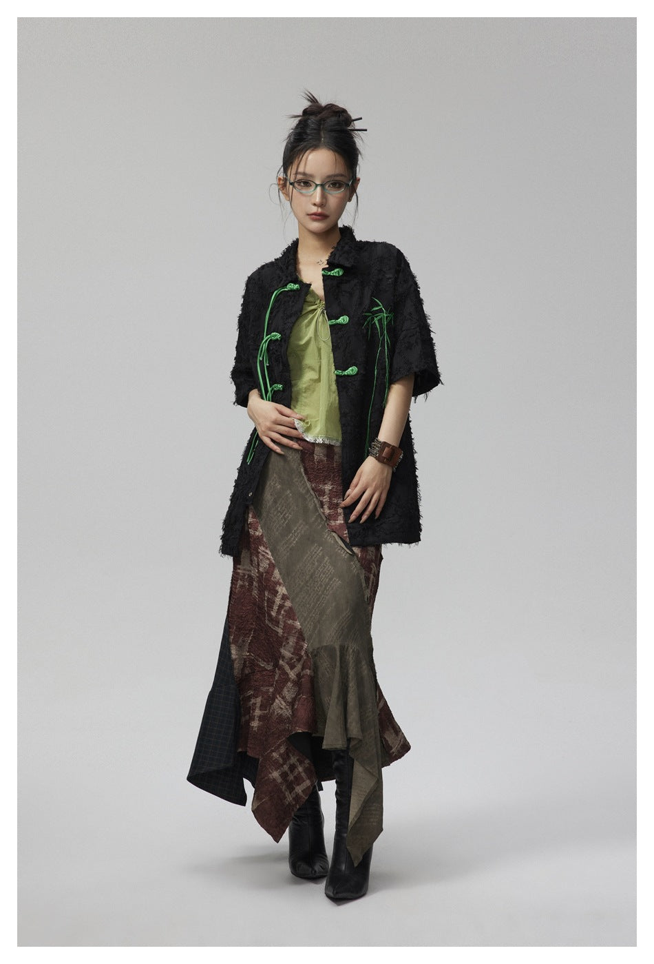 Model wearing the black textured short-sleeve shirt with green frog closures over a green top and patchwork skirt