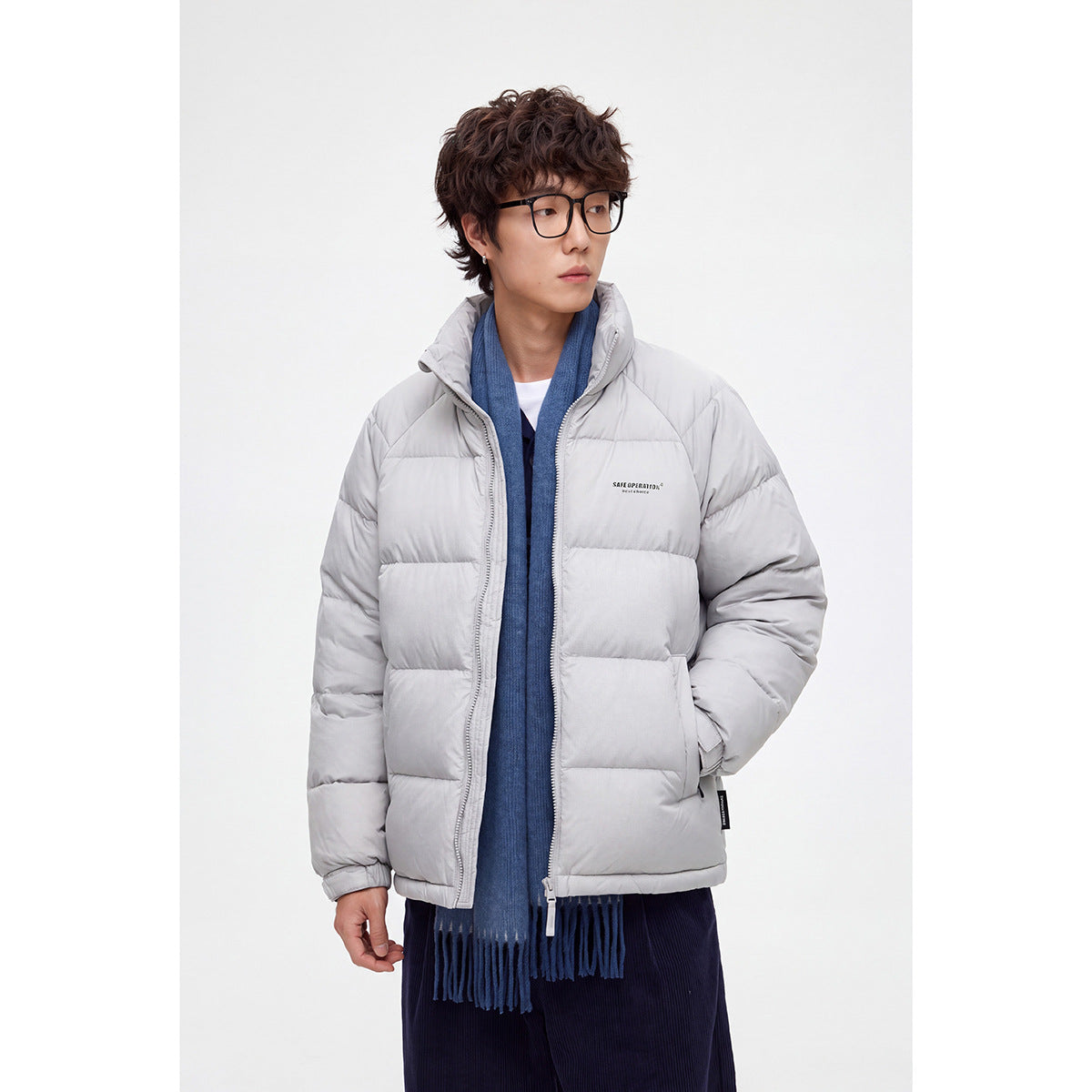 Model wearing a light gray quilted puffer jacket with a high collar, layered over a blue scarf.