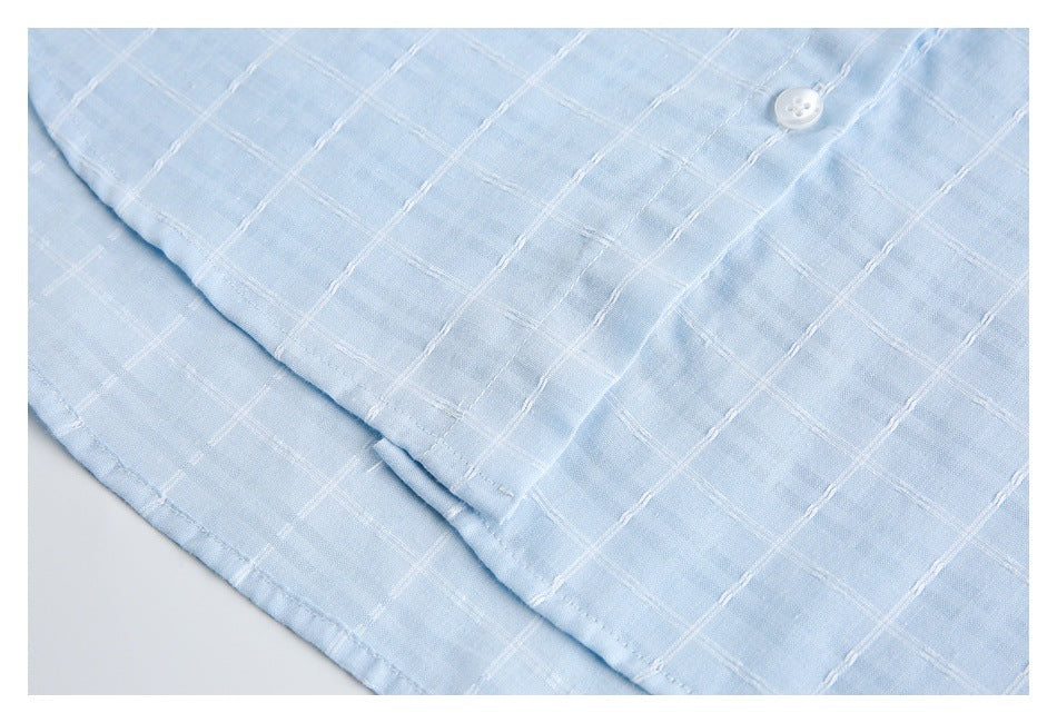 Close-up of pale blue shirt fabric with white windowpane stitching, a white button, and a stitched edge.
