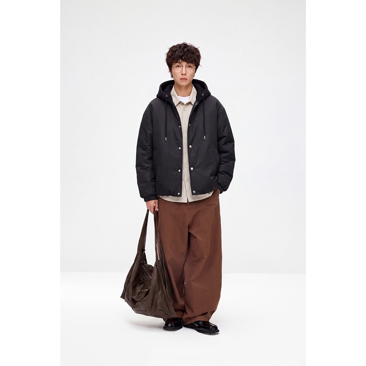 Model wearing a black hooded snap-front jacket with drawstrings and front pockets.