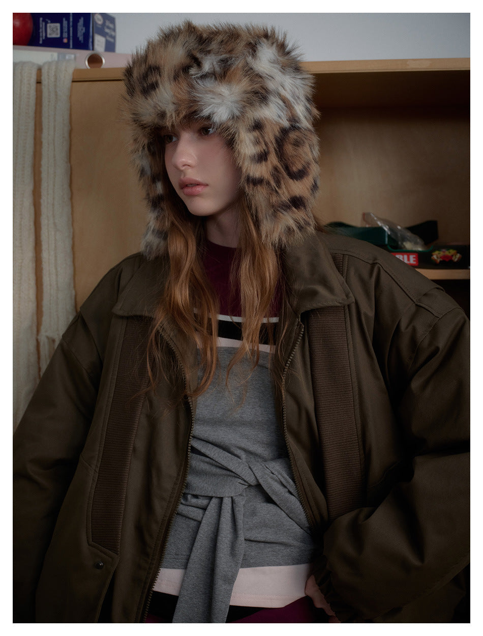 Close view of a model wearing an olive-brown jacket with ribbed panels and a spotted faux-fur trapper hat.