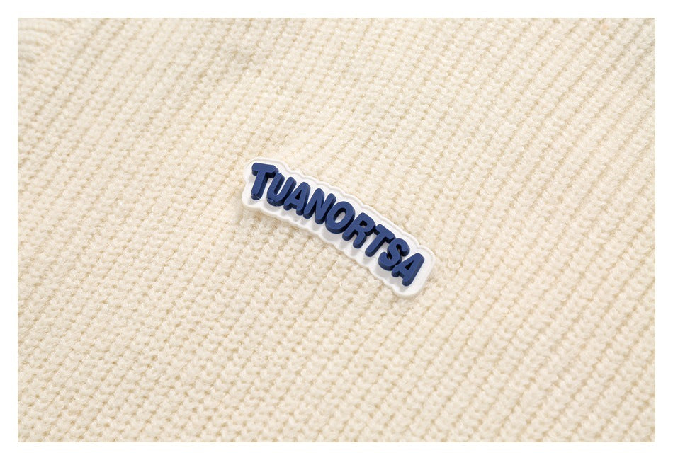 Close-up of a blue-and-white TUANORTSA patch on the ivory sweater’s textured knit.