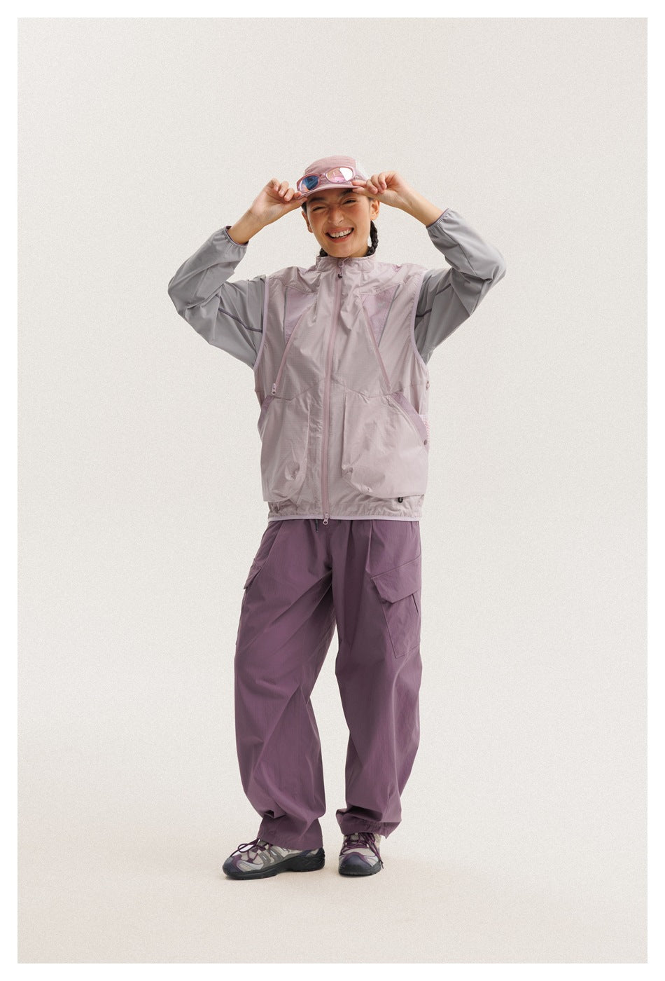 Person models a pale mauve zip jacket with gray sleeves and large pockets, plum cargo pants, and a pink cap.
