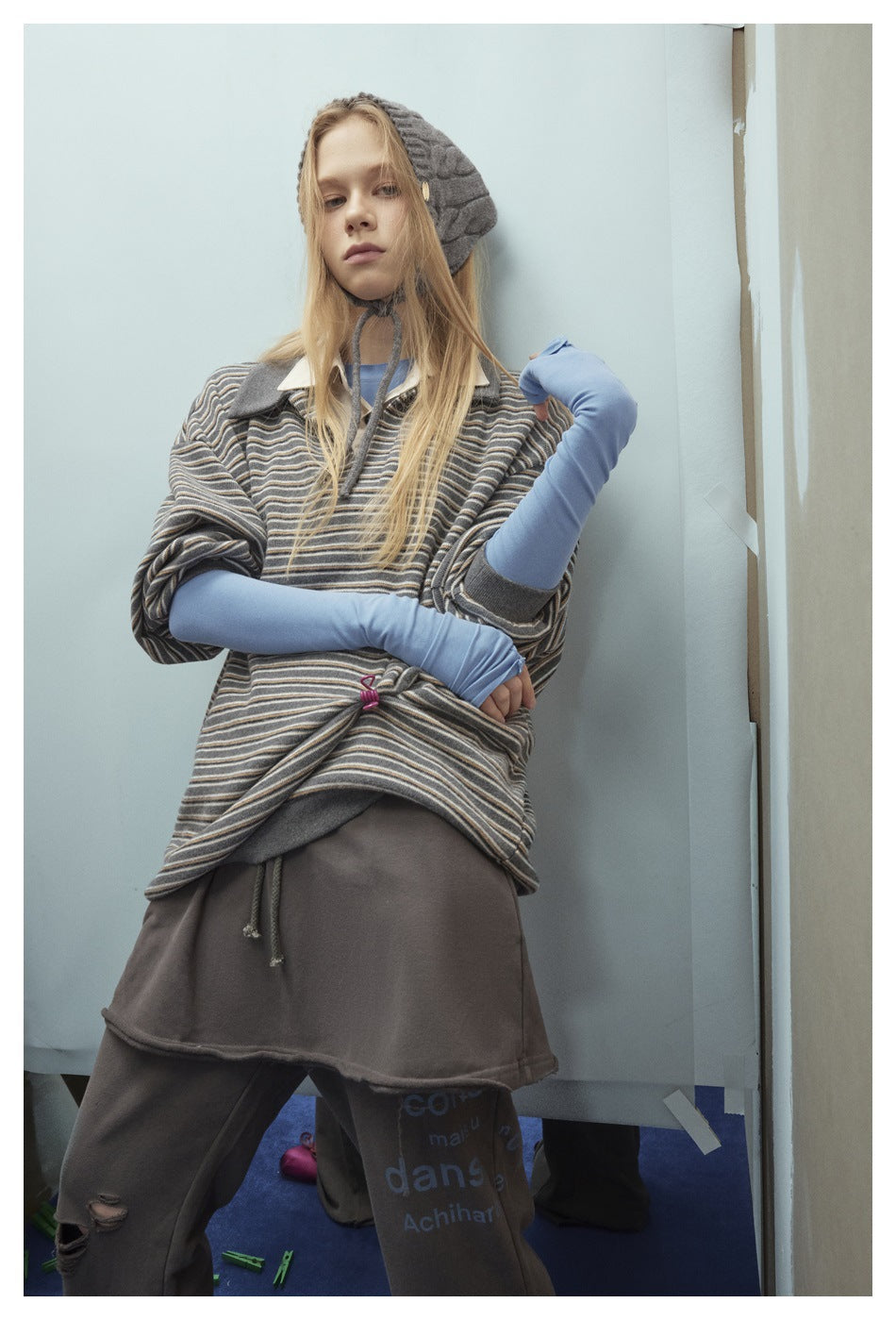 Model wearing an oversized gray striped short-sleeve collared pullover over blue sleeves, with dark gray bottoms.