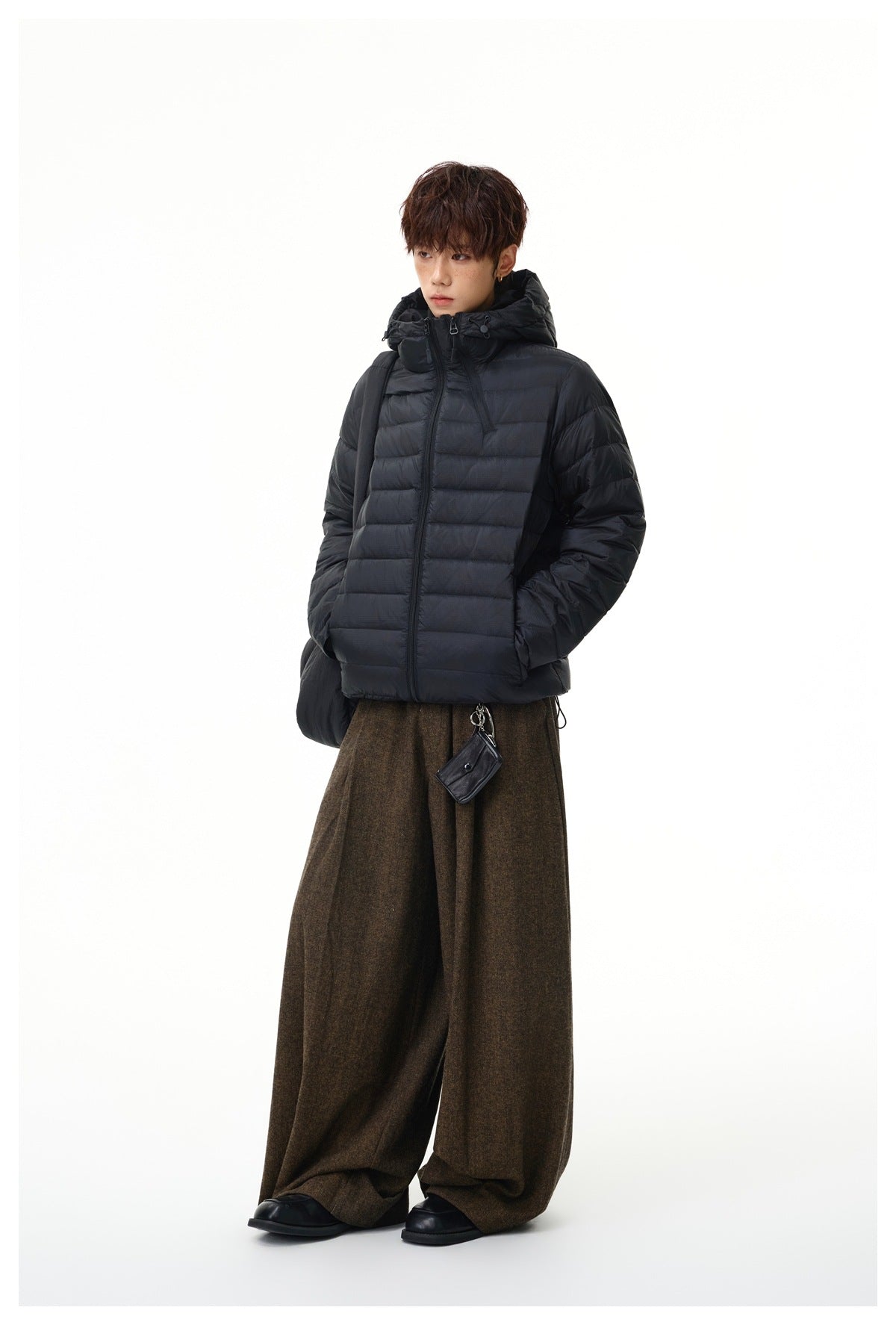 Model wearing a black hooded quilted jacket with wide brown trousers, shown at a slight angle.