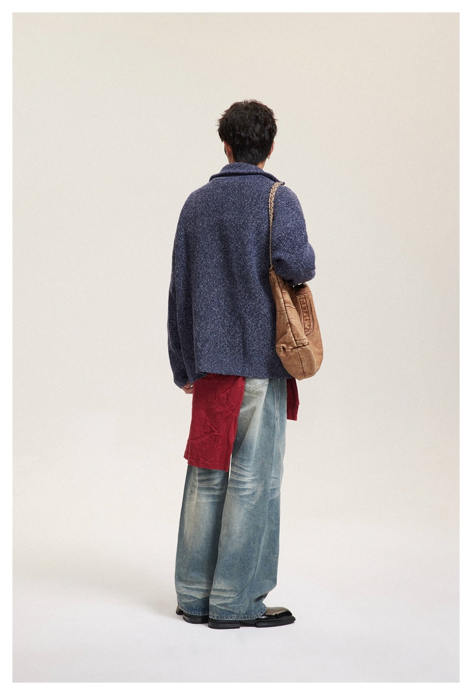 Back view of model in navy knit zip sweater with red layer, wide-leg jeans and brown shoulder bag