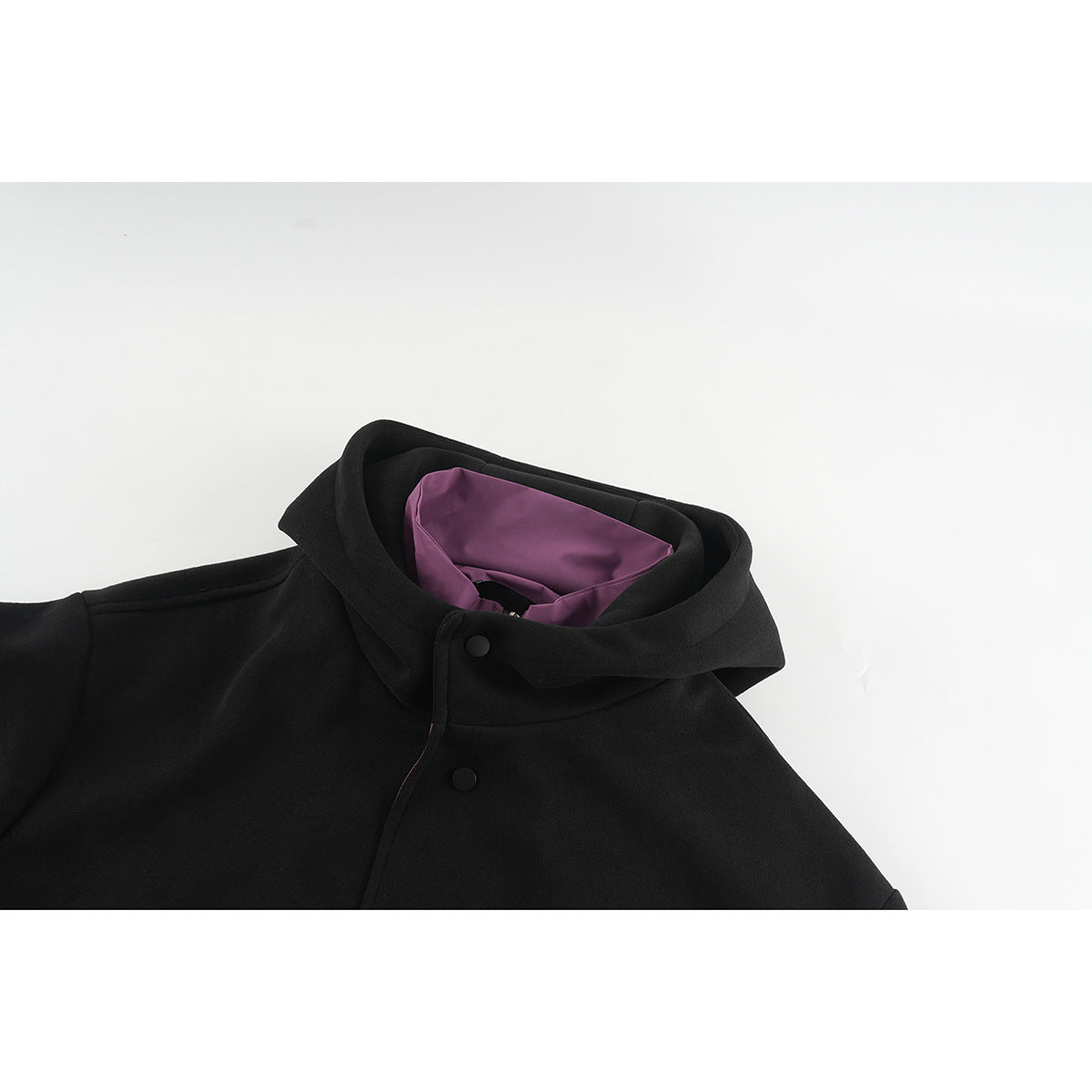 Close-up of a black hooded jacket collar with purple lining and black snap buttons.