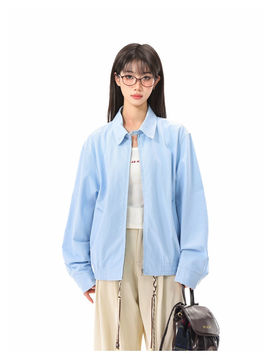 Model wearing open light blue zip jacket over a white top and cream trousers, holding a brown bag