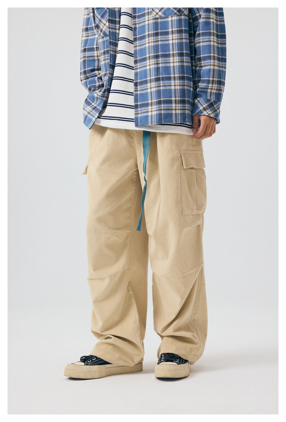 Three-quarter front view of a model wearing loose beige cargo pants with a blue drawstring and cargo pockets.