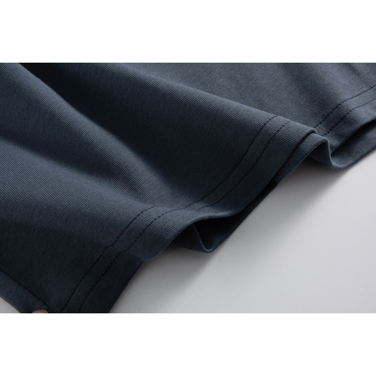 Close-up of the dark slate blue T-shirt’s fabric and double-stitched hem.