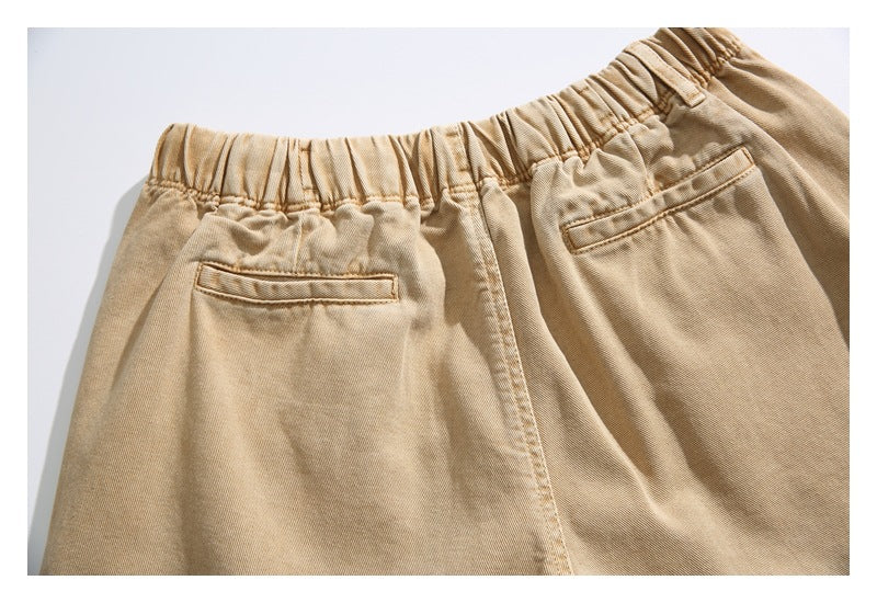 Rear waist of tan trousers with a gathered elastic waistband and two narrow welt pockets.