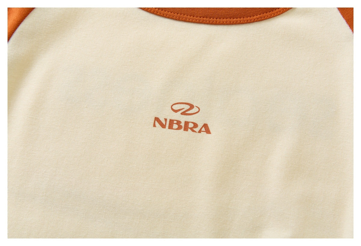 Close-up of a small rust-colored NBRA logo printed on the cream shirt front.
