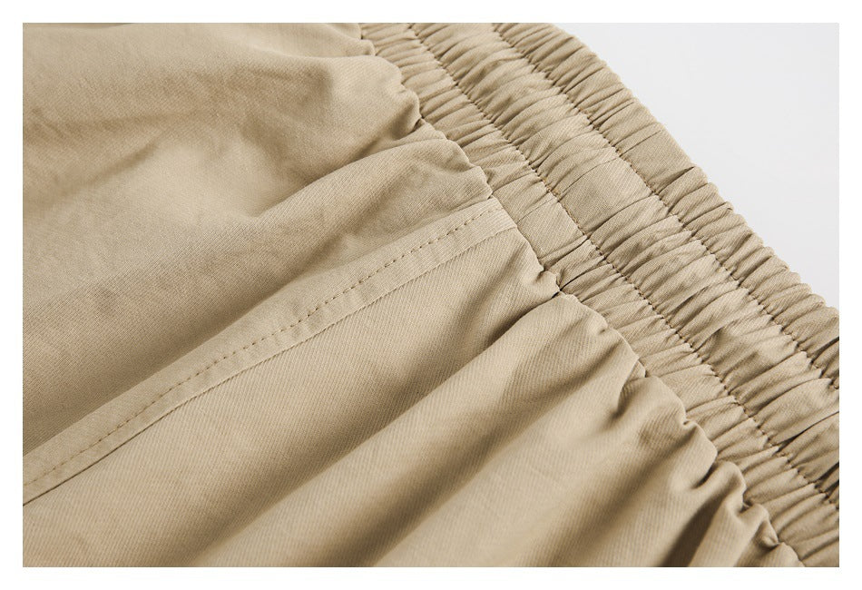 Close-up of khaki trousers showing the gathered elastic waistband and stitched pocket opening.