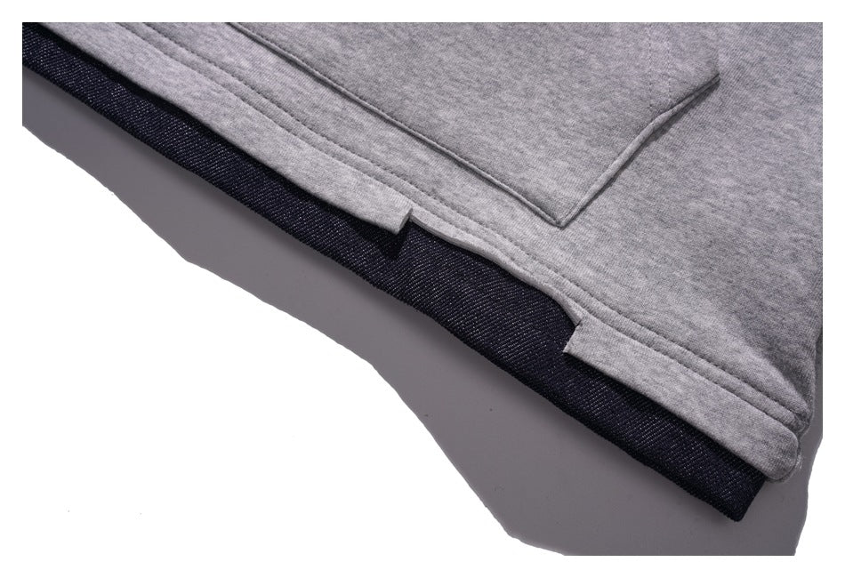 Close-up of the gray hoodie hem with small side slits and a dark contrasting layer beneath.