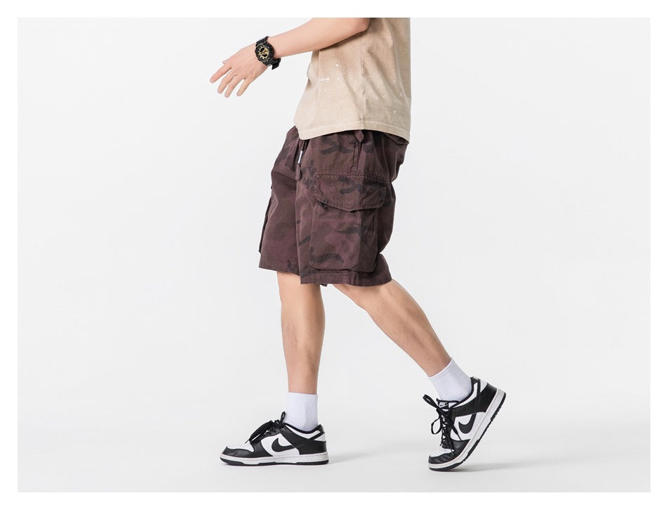 Side view of a model wearing burgundy camouflage cargo shorts with a large flap cargo pocket.