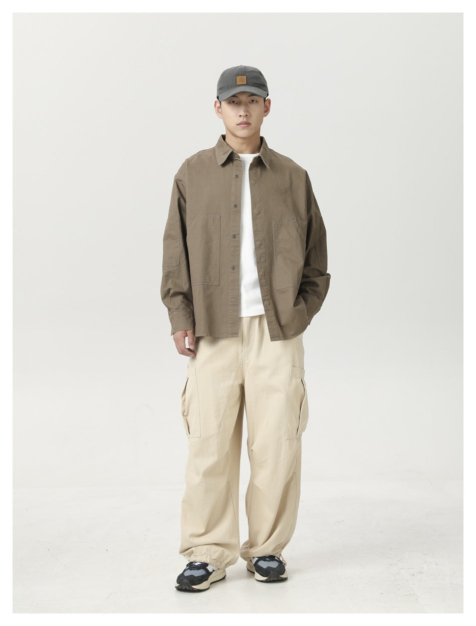 Model wearing a taupe button-front shirt over a white tee with loose cream cargo pants.