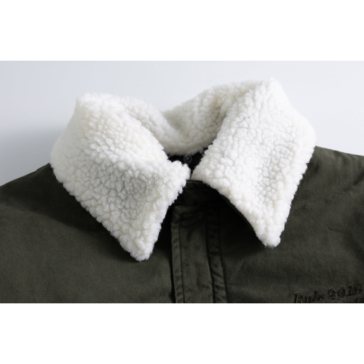 Close-up of an olive jacket with a thick white sherpa collar and dark embroidered lettering.