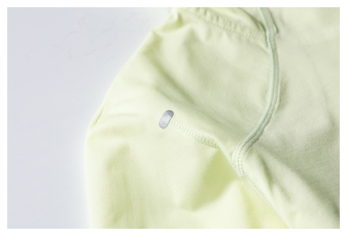 Close-up of pale yellow-green garment fabric with curved stitching and a small reflective tab.