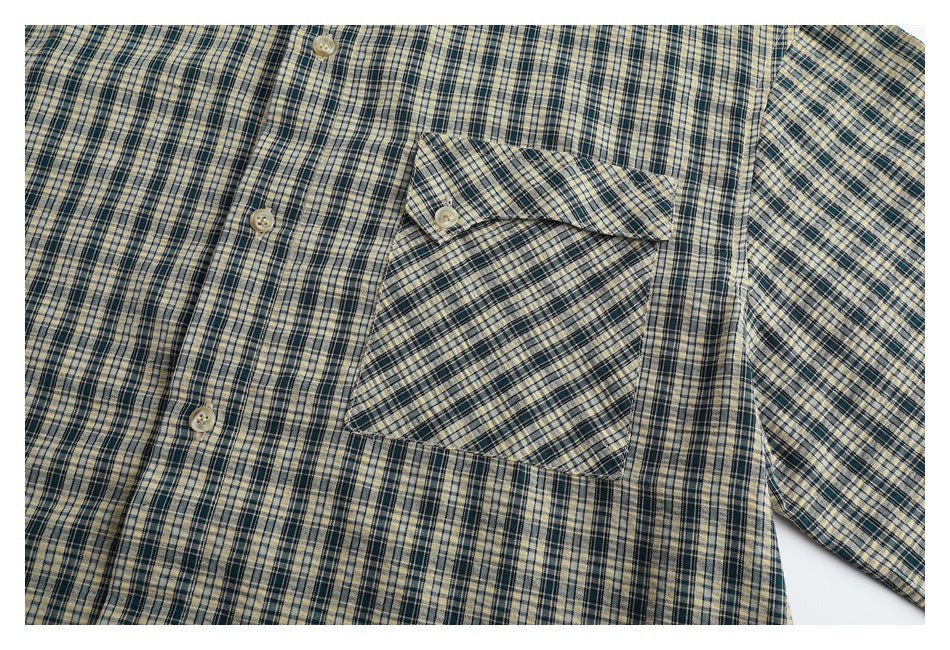Close-up of a cream and dark plaid button-up shirt showing its button placket and chest pocket.