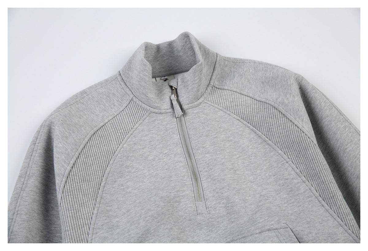 Close-up of the light gray sweatshirt front, showing its stand collar, short zipper, ribbed panels, and kangaroo pocket.