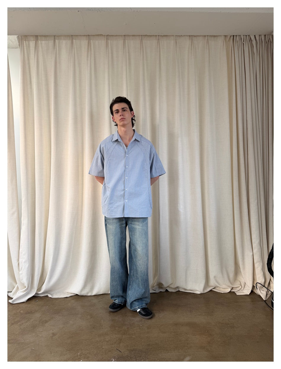 Full-length front view of a person wearing a light blue striped short-sleeve button-up shirt with jeans.