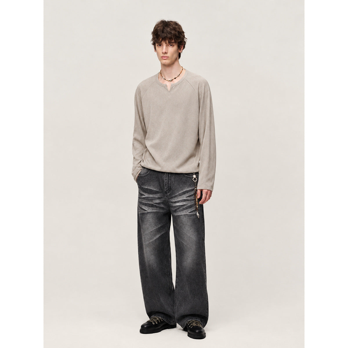 Model wearing a light beige long-sleeve top and charcoal wide-leg jeans with faded stripe details.