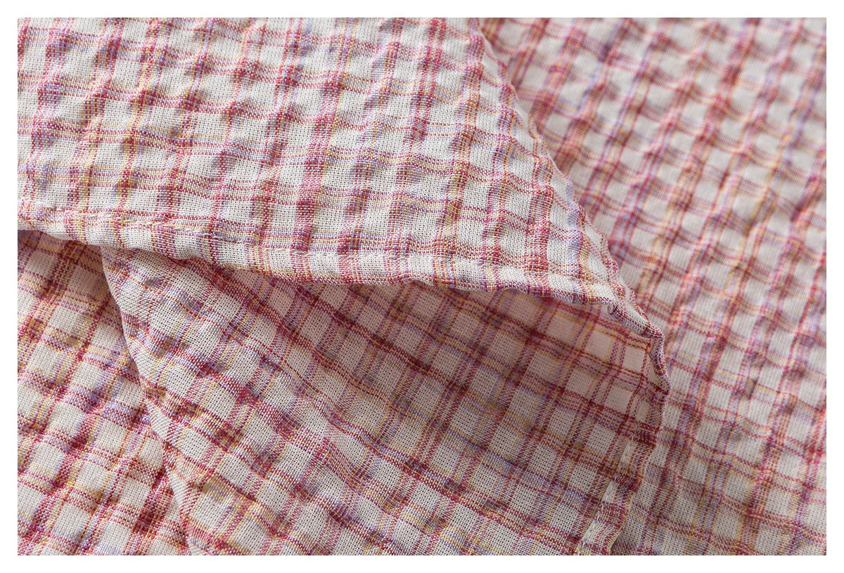 Close-up of a folded, stitched edge on cream plaid fabric with pink, red, and muted yellow lines.