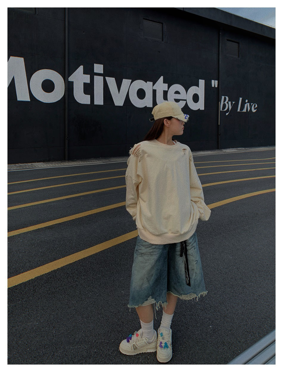 Model standing on a road in an oversized distressed khaki sweatshirt, denim shorts, cap and sneakers