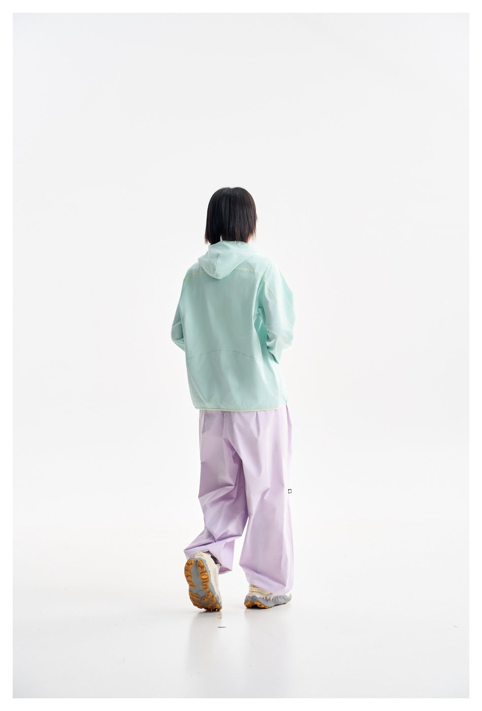 Rear view of a model wearing a mint hooded jacket and loose lavender pants.