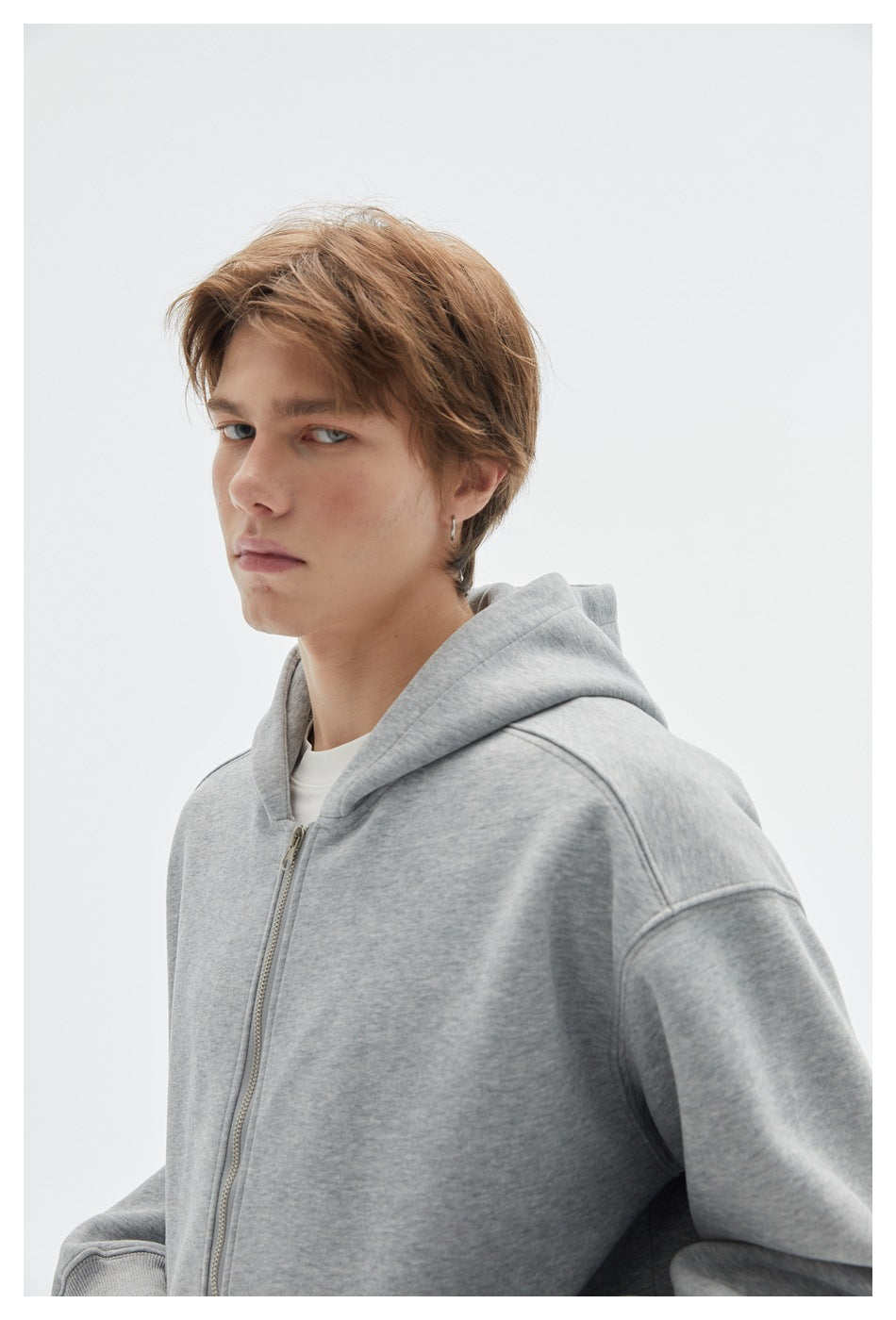 Close-up of a model wearing a light gray zip hoodie, showing the hood, zipper and shoulder seams.