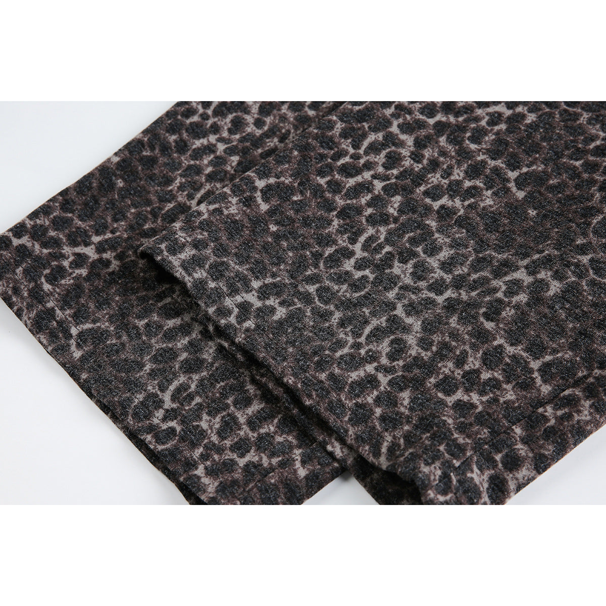 Close-up of overlapping fabric panels on dark brown and black leopard-print trousers.