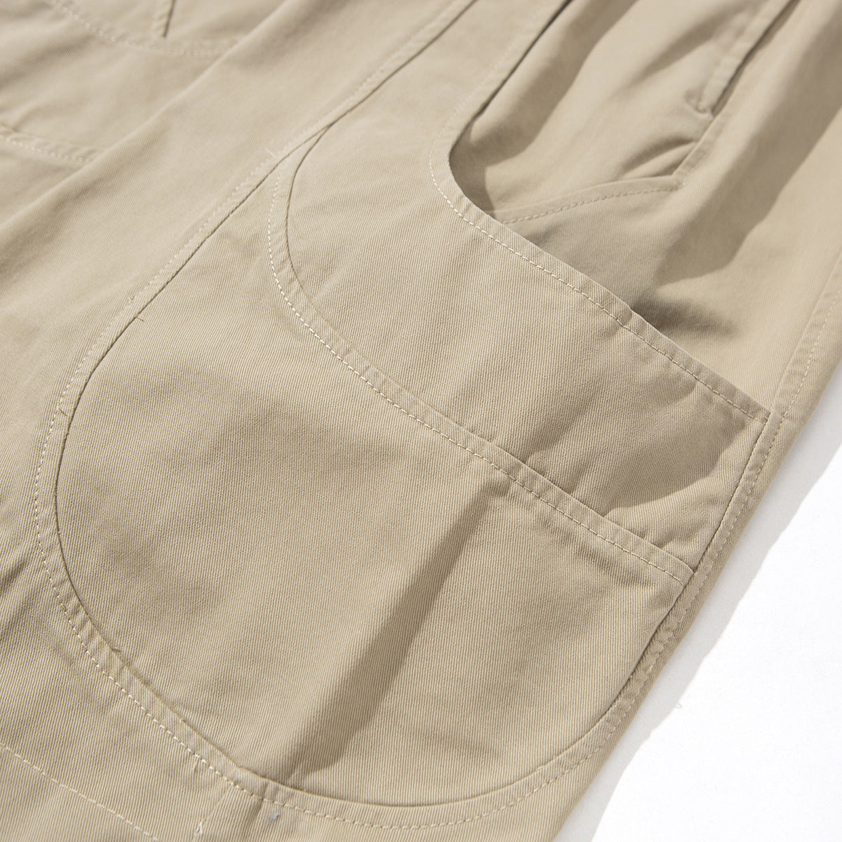 Close-up of beige pants showing a large curved patch pocket and a slanted side pocket.