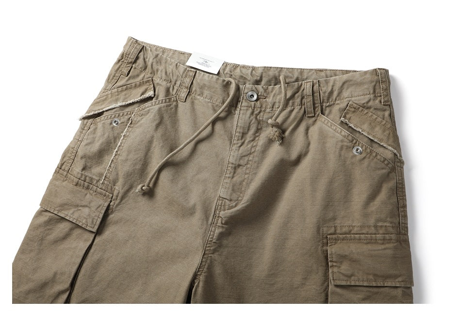 Close-up of taupe cargo shorts showing the drawstring waist, button closure and large flap pockets.