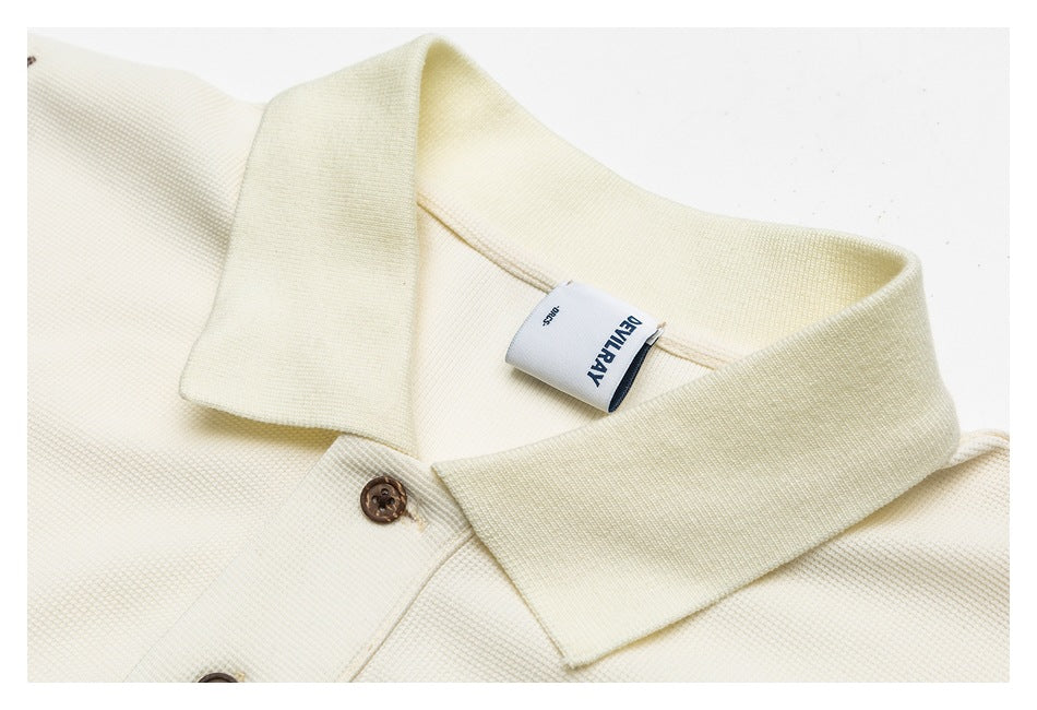 Close-up of an ivory shirt collar, brown buttons, and sewn neck label.