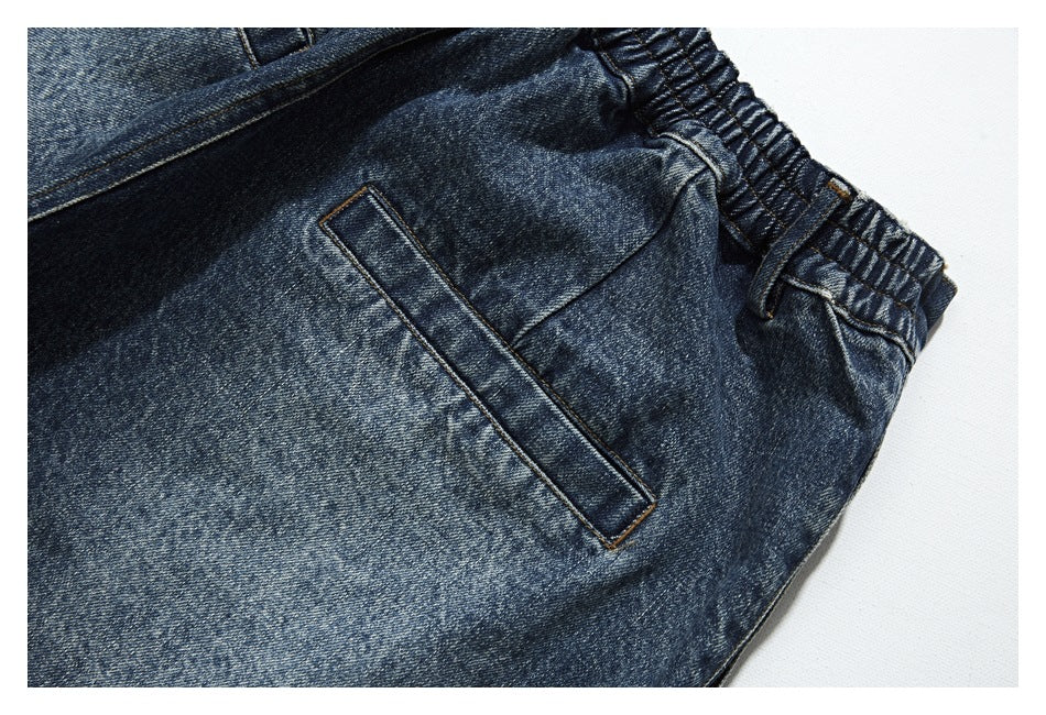 Close-up of dark blue washed denim trousers showing the gathered waistband and a slanted pocket opening.