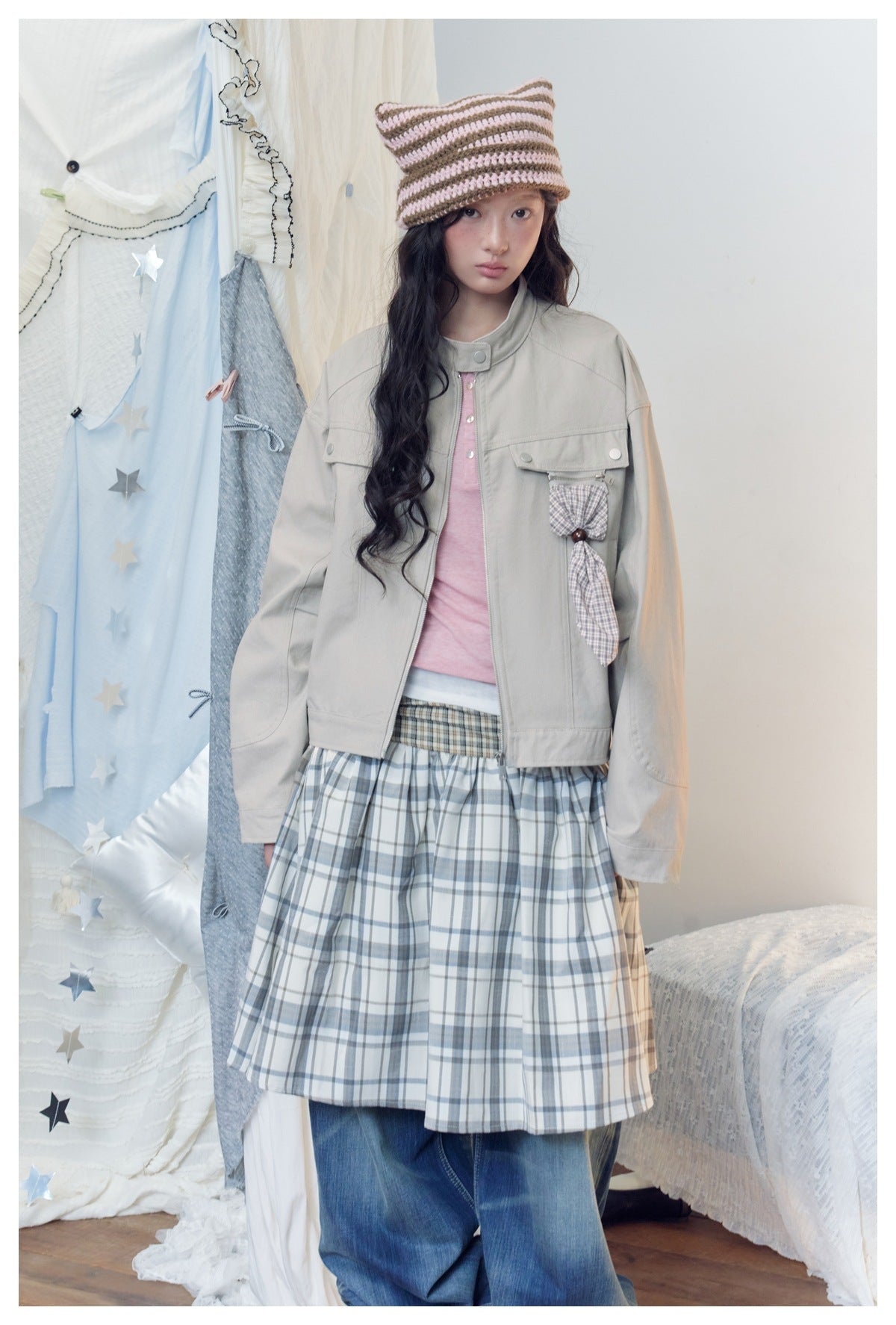 Model in a light gray jacket with plaid bow detail and a gray-and-cream plaid skirt over jeans.