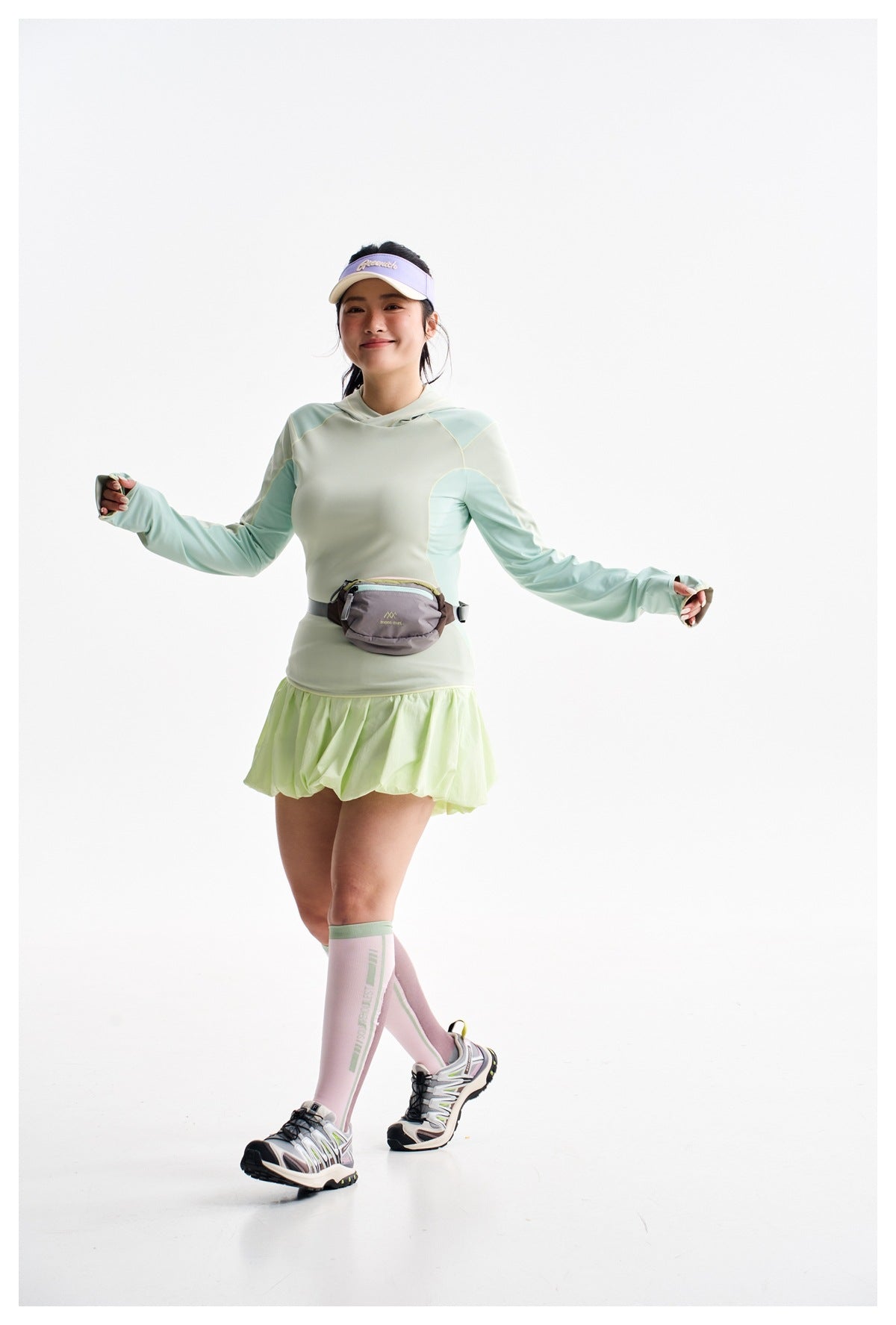 Model wearing a pale mint color-block hooded top and lime bubble-hem tennis skirt, with a waist pack.